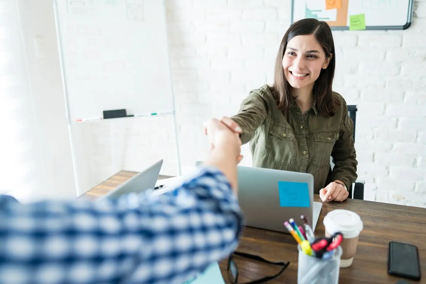 Улыбающаяся бизнесвумен пожимает руку коллеге во время офисной встречи.